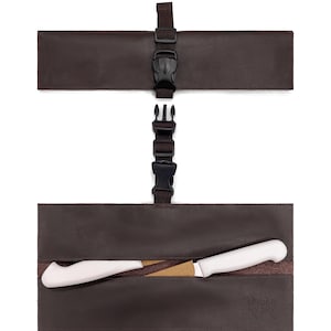 以下が含まれることがあります： 黒いバックル留めが付いた茶色の革製ナイフロール。ロールは開いており、白い柄のナイフが見えます。「UNDER NY SKY」の文字がロールに表示されています。