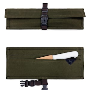 以下が含まれることがあります： 濃い緑色のキャンバス製ナイフロール。茶色のストラップとバックル留めが付いています。ロールは閉じた状態と開いた状態の両方で表示され、白い柄のナイフと木製の鞘が明らかになります。ナイフロールには、「UNDER AT THE」と書かれた小さな濃い青色のタグが付いています。