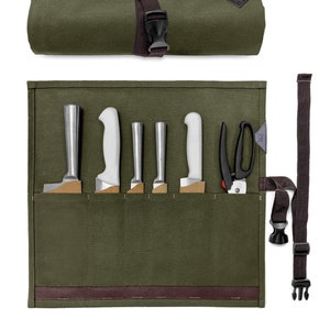 May include: A green canvas knife roll with a brown leather strap and buckle. The roll has six slots for knives and one slot for shears. The roll is rolled up and secured with the strap.