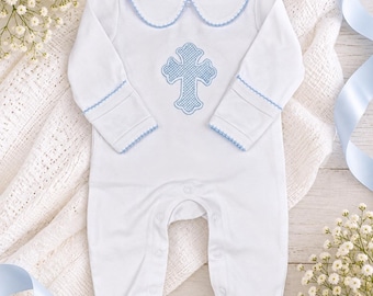 May include: A white long-sleeved footed romper featuring a Peter Pan collar with light blue trim. The chest displays a light blue cross embroidery with a cross-stitch pattern. The sleeve cuffs have matching light blue trim, and the garment includes a snap-button closure along the front and inner legs.