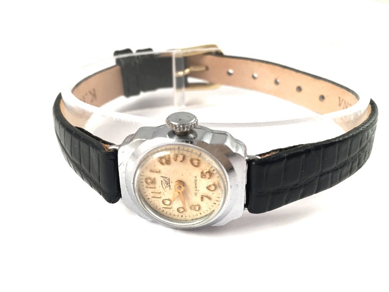 May include: A silver wristwatch with a black leather band. The watch face is cream colored with black Arabic numerals and a gold-colored second hand.