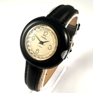 May include: A black and white wristwatch with a round face and a black leather band. The watch face has a white background with black numbers and hands. The watch face also has the word "Cza-Rad" printed on it.