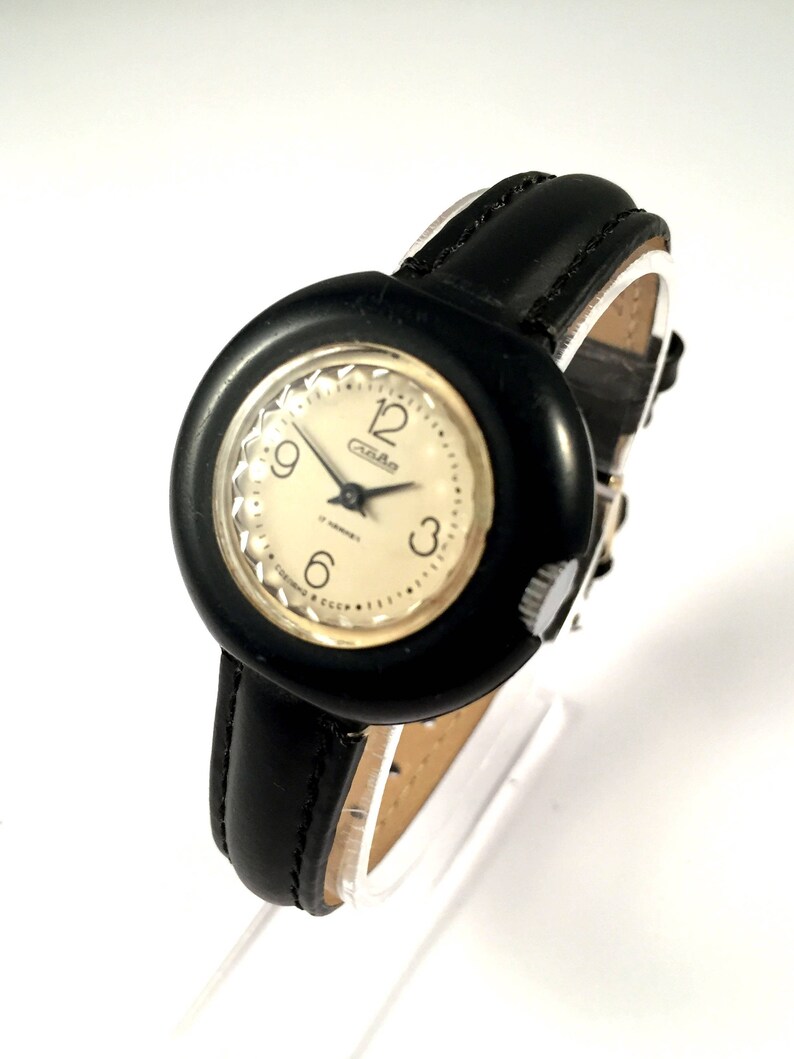 May include: A black and white wristwatch with a round face and a black leather band. The watch face has a white background with black numbers and hands. The watch face also has the word "Cza-Rad" printed on it.
