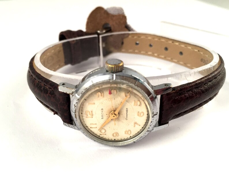May include: A silver wristwatch with a white face and black leather strap. The watch face has black Roman numeral hour markers and a gold second hand. The watch face also has the word "СССР" printed on it.