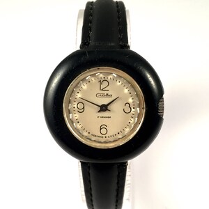 May include: A black wristwatch with a round, black face and a black leather band. The watch face has white numbers and hands, and the text "Слава 17 камней Сделано в СССР" is printed on the face.