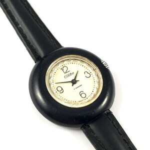 May include: A black wristwatch with a white face and black leather band. The watch face has black numbers and hands, and the text "17 камней" and "Сделано в СССР".