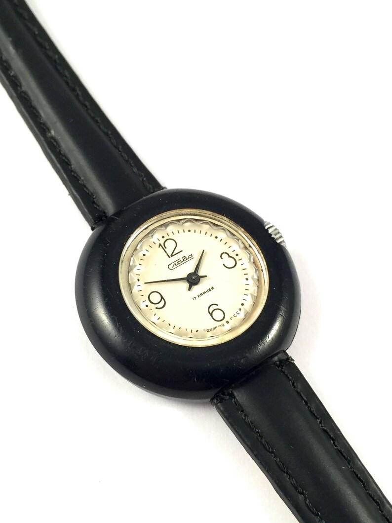 May include: A black wristwatch with a white face and black leather band. The watch face has black numbers and hands, and the text "17 камней" and "Сделано в СССР".