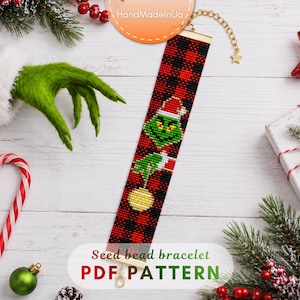 Puede incluir: Una pulsera rectangular de cuentas con un patrón de cuadros rojos y negros, que muestra un personaje verde con gorro de Papá Noel sosteniendo un adorno amarillo. Incluye un cierre de metal dorado y una cadena de extensión ajustable.