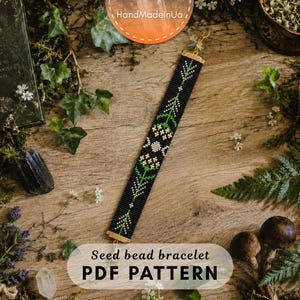May include: A seed bead bracelet featuring a black background with a repeating pattern of green stems, white flowers, and a central triple moon symbol. The bracelet is finished with gold-toned metal end bars and a small clasp at the top.