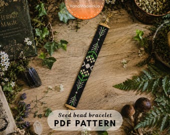 May include: A seed bead bracelet featuring a black background with a repeating pattern of green stems, white flowers, and a central triple moon symbol. The bracelet is finished with gold-toned metal end bars and a small clasp at the top.