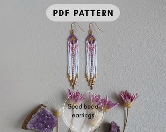 May include: Two beaded earrings with a white, pink, gold, and purple design. The earrings are long and dangle, with a teardrop shape. The image also includes the text "PDF PATTERN" and "Seed bead earrings".