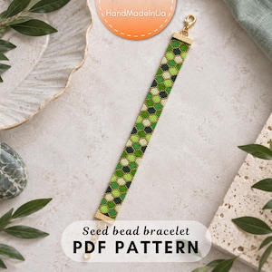 Puede incluir: Una pulsera larga y estrecha de cuentas de semillas con un patrón geométrico de panal repetitivo en tonos verde lima, verde bosque, crema y negro. La pulsera está terminada con terminales de metal dorado y un cierre de mosquetón.