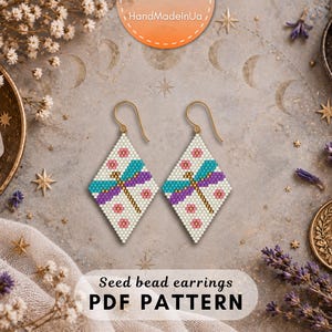 May include: A pair of diamond-shaped seed bead earrings featuring a dragonfly design with teal and purple wings, a brown body, and small pink flower accents on a white background, suspended from gold-toned metal ear wires for pierced ears.