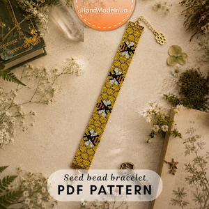 Puede incluir: Una pulsera de cuentas con un patrón repetitivo de panal en amarillo y naranja con motivos de abejas en blanco y negro. La pulsera incluye una cadena extensora de metal dorado con un pequeño dije en forma de panal al final del cierre.