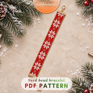 May include: A rectangular seed bead bracelet featuring a repeating pattern of white snowflakes on a red background with small gold accents. The bracelet is finished with a gold-toned metal clasp at one end and a matching gold-toned metal bar at the other.
