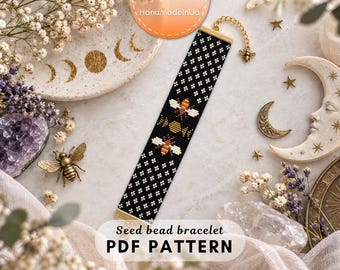 May include: A rectangular seed bead bracelet featuring a black background with a repeating white floral pattern, two central honeybee motifs, and a moon phase design. The bracelet includes a gold-tone metal clasp and a small bee charm.