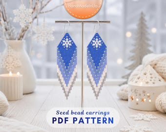 May include: A pair of long, diamond-shaped seed bead earrings featuring a blue and white gradient pattern with a white snowflake design at the top. The earrings hang from silver-toned hooks and display a fringe-like bottom edge.