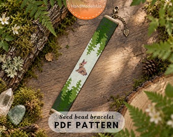 May include: A rectangular seed bead bracelet featuring a forest landscape pattern with green pine trees and a small brown rabbit on a light background. The bracelet includes bronze-toned metal end caps and a chain extension with a leaf-shaped charm.