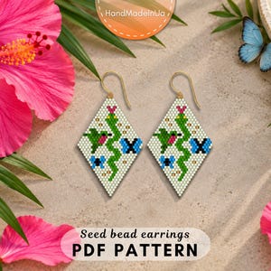 May include: A pair of diamond-shaped seed bead earrings featuring a green snake, a small hummingbird, and blue butterflies on a white background. The earrings are suspended from gold-toned metal hooks and display a detailed, colourful pixelated pattern.