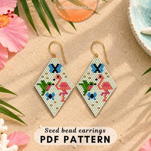 Può includere: Un paio di orecchini a forma di diamante realizzati con perline, caratterizzati da un motivo pixelato con un fenicottero rosa, un colibrì verde e farfalle blu su sfondo chiaro, appesi a ganci in metallo dorato con etichetta PDF sotto.