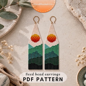 May include: A pair of long, rectangular seed bead earrings featuring a landscape design. The pattern displays a gradient of green and black mountains at the base, topped with a white sky and a circular orange and yellow sun. Gold-toned ear wires.