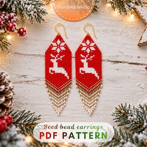 May include: A pair of long, diamond-shaped seed bead earrings featuring a red background with a white reindeer and snowflake pattern. The bottom edges have a fringe of gold and white beads. The text "Seed bead earrings PDF PATTERN" is visible.