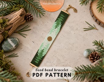 May include: A rectangular seed bead bracelet featuring a forest landscape design with dark green pine trees, a light green sky, and a golden sun. The bracelet has gold-toned metal end bars, a lobster claw clasp, and a small leaf-shaped charm.