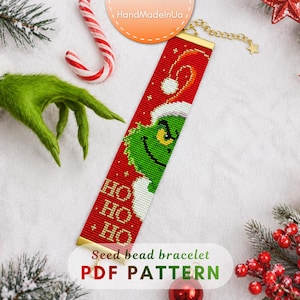 Op de afbeelding: Een rechthoekige kralenarmband met een rode achtergrond, een groen personage met een witte kerstmuts en de tekst HO HO HO in goud. De armband heeft gouden metalen eindstukken en een kettingverlenging met een kleine ster als bedel.