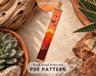 May include: A rectangular seed bead bracelet featuring a desert landscape pattern with a yellow sun, orange sky, and dark red ground. The design includes small bird silhouettes and cactus shapes. It has gold-toned metal end caps and a lobster clasp.