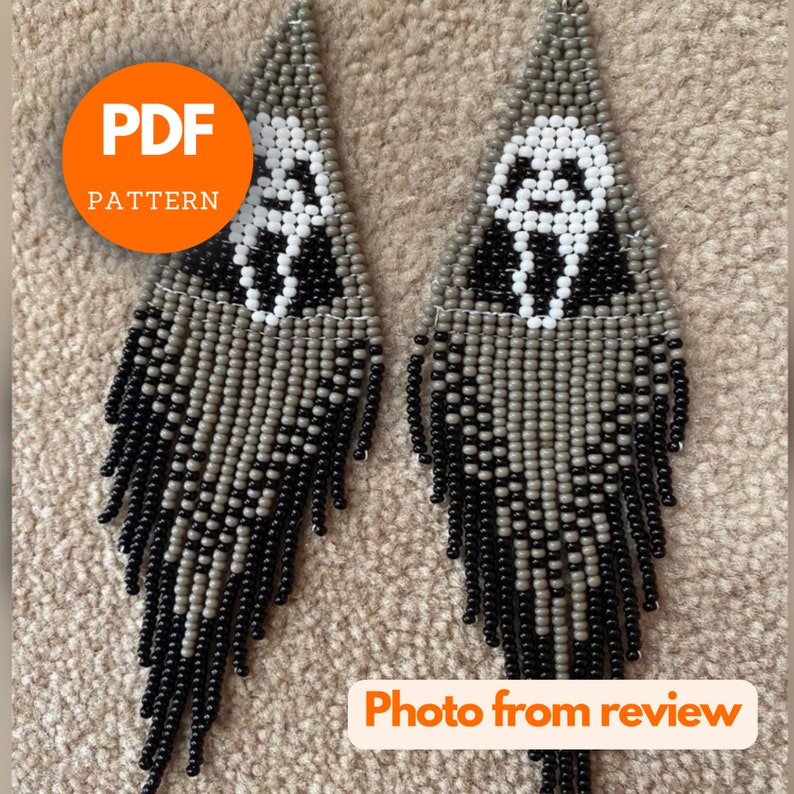 May include: A pair of beaded earrings with a black and gray color scheme. The earrings feature a white skull design with a scream face. The earrings are long and dangle.