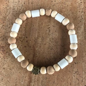 Op de afbeelding: Een houten kralen armband met witte en bruine kralen en een gouden pootprint bedel.