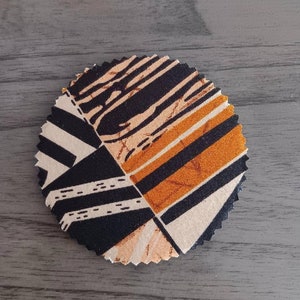 May include: A round fabric coaster with a geometric pattern in black, white, orange, and brown.