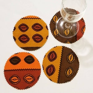 May include: Set of four round fabric coasters with a brown, orange, and red geometric pattern. The coasters have a scalloped edge.
