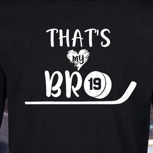 May include: Black long-sleeved shirt with white text that reads 'That's My Bro' with a heart and hockey puck graphic.