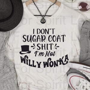 May include: A white t-shirt with the black text "I don't sugar coat shit, I'm not Willy Wonka". The shirt is styled with grey jeans, white trainers, a black hat, and a grey cardigan. Sunglasses and a necklace are also present.
