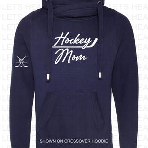 K&ouml;nnte beinhalten: Marineblauer Crossover-Hoodie mit einem wei&szlig;en Aufdruck, der "Hockey Mom" mit einem Hockeyschl&auml;ger unter dem Wort "Hockey" sagt. Der Aufdruck befindet sich auf der Vorderseite des Hoodies. Der Hoodie hat eine Kapuze mit Kordelzug und eine K&auml;ngurutasche.
