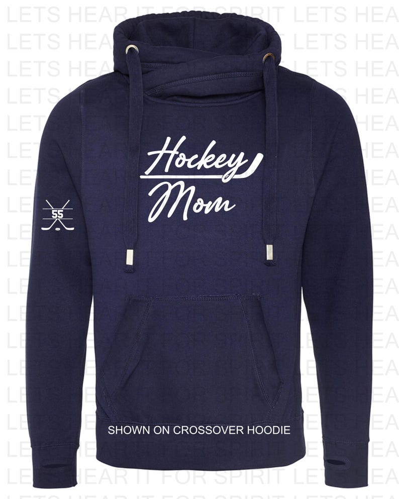 K&ouml;nnte beinhalten: Marineblauer Crossover-Hoodie mit einem wei&szlig;en Aufdruck, der "Hockey Mom" mit einem Hockeyschl&auml;ger unter dem Wort "Hockey" sagt. Der Aufdruck befindet sich auf der Vorderseite des Hoodies. Der Hoodie hat eine Kapuze mit Kordelzug und eine K&auml;ngurutasche.