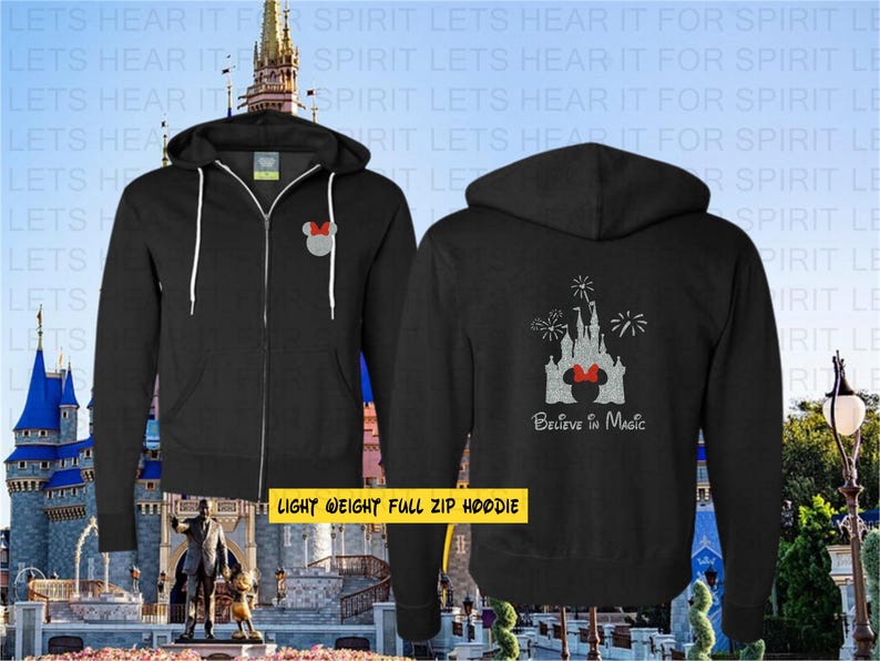 May include: A black full-zip hoodie featuring a small grey Minnie Mouse icon on the left chest. The back displays a large grey castle graphic with fireworks and the text "Believe in Magic" in white script lettering below the castle design.