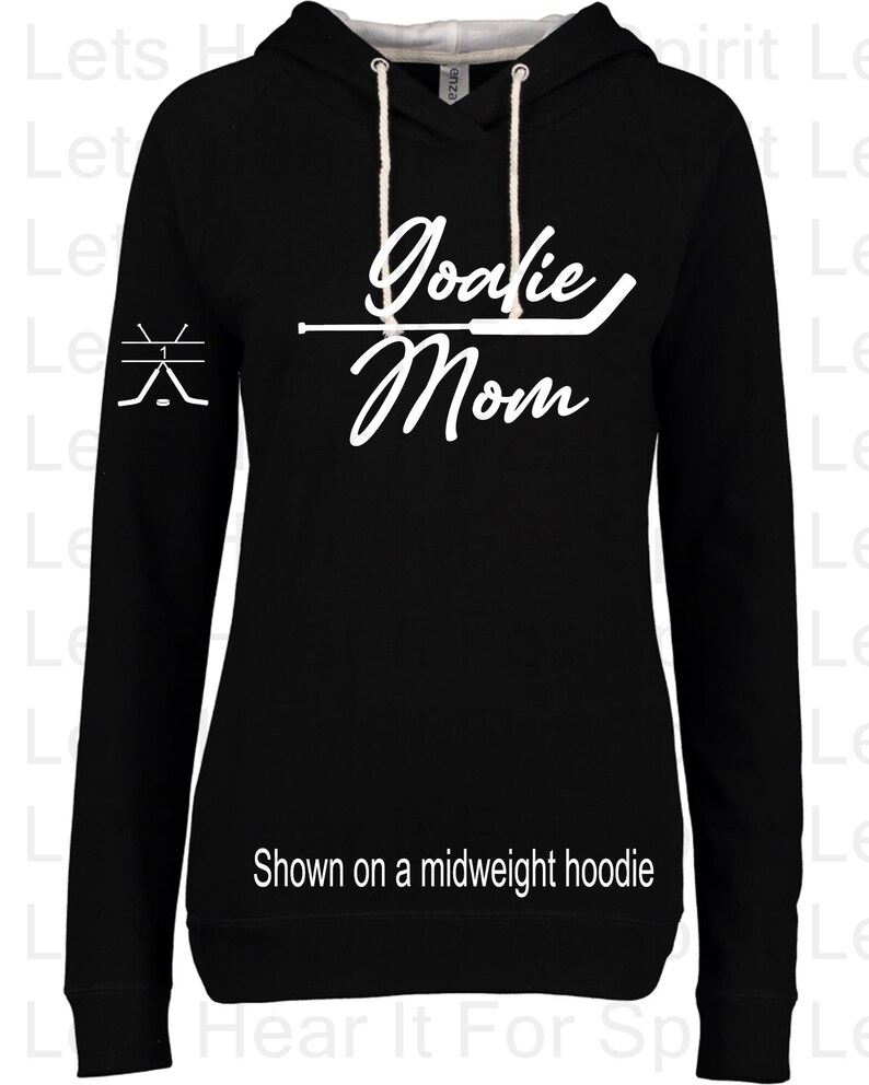 Puede incluir: Sudadera con capucha negra con texto blanco que dice "Goalie Mom" y un gr&aacute;fico de un palo de hockey. La sudadera se muestra en una modelo.