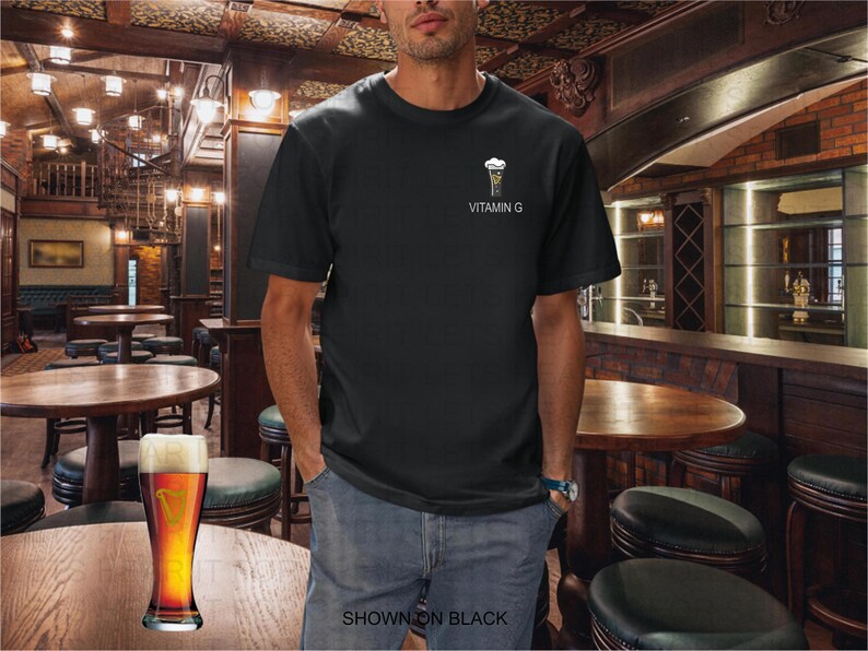 K&ouml;nnte beinhalten: Schwarzes T-Shirt mit einer kleinen Grafik eines Bierglases und dem Text "VITAMIN G". Das Bild zeigt einen Mann in einer Bar, mit einem Bier auf dem Tisch. Der Text "SHOWN ON BLACK" steht unten.