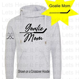 K&ouml;nnte beinhalten: Grauer Crossover-Hoodie mit einer schwarzen Grafik, auf der "Goalie Mom" mit einem Hockeyschl&auml;ger-Design steht. Die Grafik befindet sich auf der Vorderseite des Hoodies und auf dem linken &Auml;rmel befindet sich eine kleinere Hockeyschl&auml;ger-Grafik.