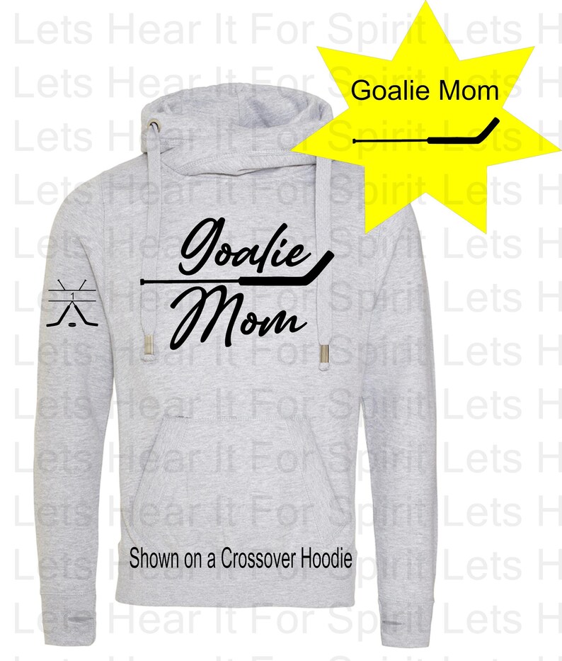 K&ouml;nnte beinhalten: Grauer Crossover-Hoodie mit einer schwarzen Grafik, auf der "Goalie Mom" mit einem Hockeyschl&auml;ger-Design steht. Die Grafik befindet sich auf der Vorderseite des Hoodies und auf dem linken &Auml;rmel befindet sich eine kleinere Hockeyschl&auml;ger-Grafik.