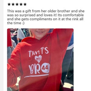 K&ouml;nnte beinhalten: Roter Hoodie mit wei&szlig;em Text, der "That's My Bro 44" lautet. Der Text ist in Herzform mit einer Grafik eines Hockeyscheiben.
