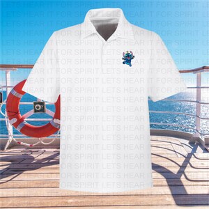 Puede incluir: Camiseta polo blanca con un personaje de dibujos animados azul que lleva un sombrero y gafas de sol en el pecho izquierdo. El personaje sostiene una tabla de surf. La camiseta tiene el texto "Lets Hear It For Spirit" repetido en un patr&oacute;n.