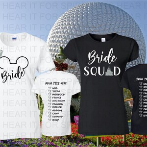 May include: Two white t-shirts with black text and graphics. One shirt says "Bride" with a Mickey Mouse ear silhouette and a diamond. The other shirt says "Your Text Here" with a list of countries and Mickey Mouse ears. A black t-shirt with white text says "Bride Squad" with a silhouette of Cinderella's castle. The shirts are in front of a backdrop of a large silver sphere.