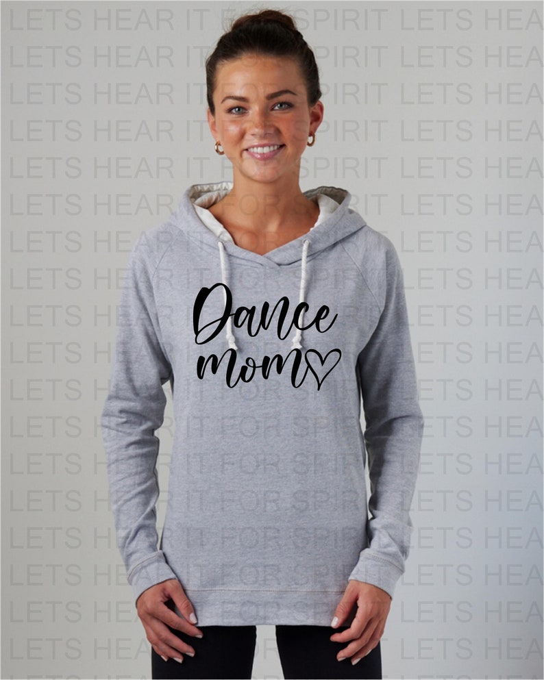 Puede incluir: Una sudadera con capucha gris con un gr&aacute;fico negro que dice "Dance Mom" con un coraz&oacute;n. La modelo lleva la sudadera y sonr&iacute;e.
