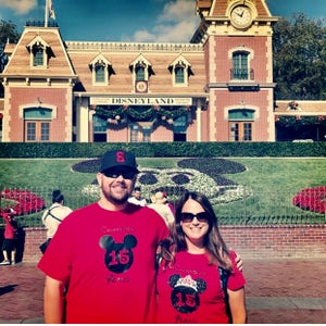 May include: A couple wearing red t-shirts with a black Mickey Mouse head and the text "Celebrating 15 Years" in front of the Disneyland entrance.