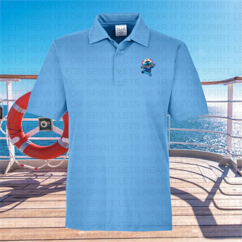 Puede incluir: Una camisa polo azul claro con cuello blanco y una peque&ntilde;a imagen bordada de un personaje azul con un sombrero rojo en el pecho izquierdo. La camisa tiene el texto "TEAM" impreso en el cuello.