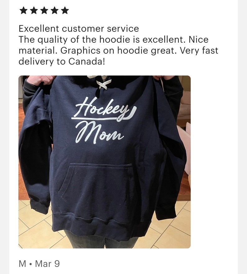 K&ouml;nnte beinhalten: Ein marineblauer Hoodie mit einem wei&szlig;en Aufdruck auf der Vorderseite, der "Hockey Mom" lautet. Der Hoodie hat eine Kapuze mit Kordelzug und eine K&auml;ngurutasche.
