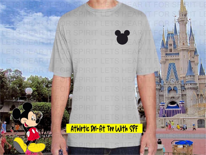 May include: A light gray athletic t-shirt with a black Mickey Mouse head silhouette on the chest. The text "Athletic Dri-fit Tee With SPF" is in a yellow rectangle at the bottom. The background shows a castle and a cartoon character.
